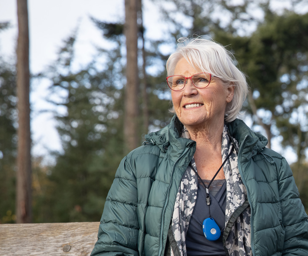stralende senior dame wandelaar in het bos met een blauwe Wuzzi Alert Pebbles om haar hals