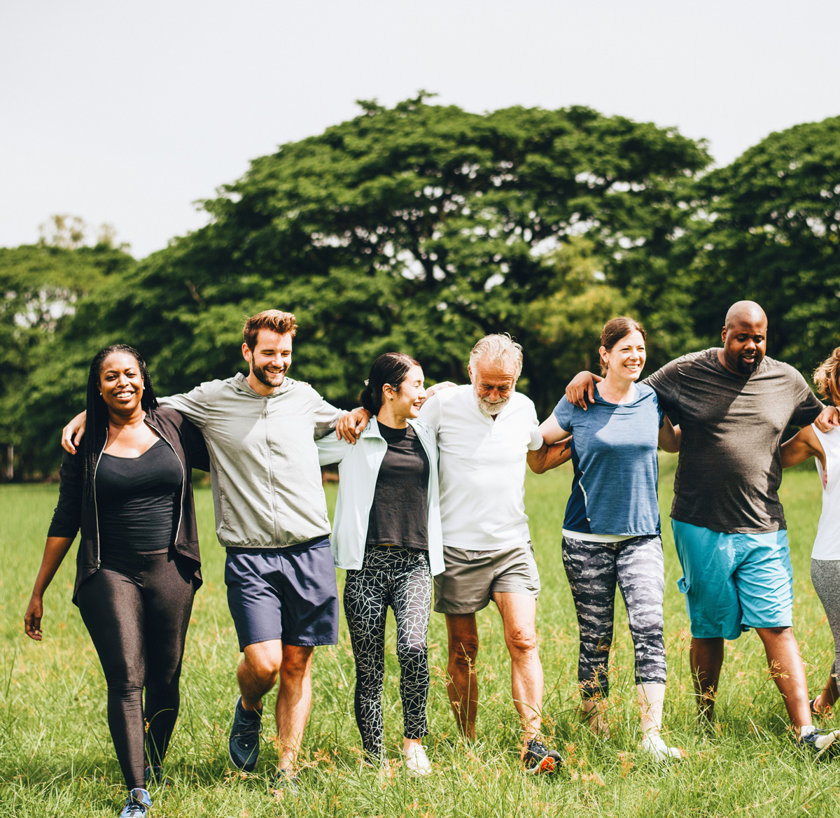 groep met mensen van verschillende leeftijden en afkomsten lopen met armen om elkaar schouders over een zomers grasveld