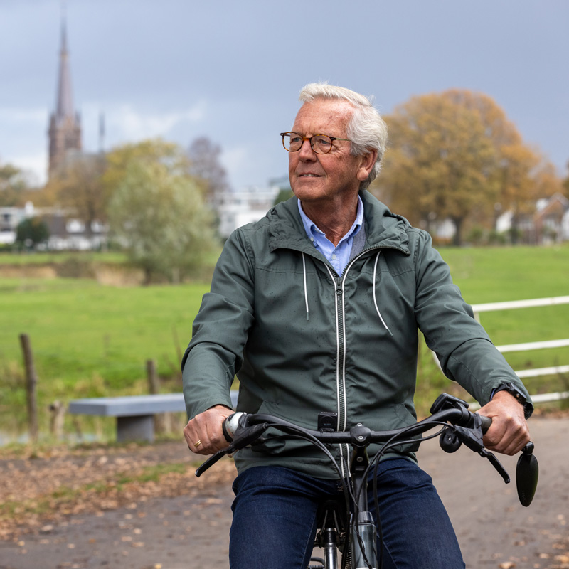 man met een fiets staat met op de achtergrond weilanden en kerk