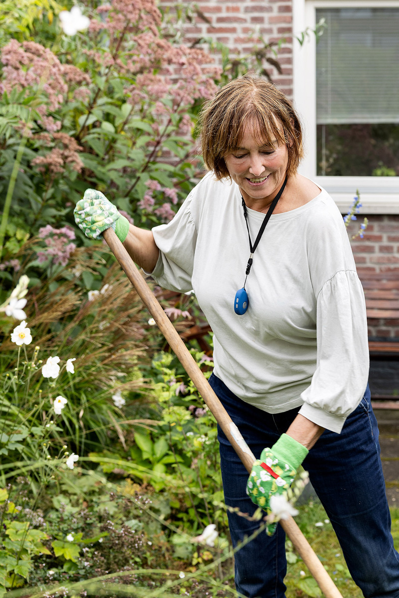 vrouw werkt in de tuin. Om haar hals draagt ze een alarmknop.